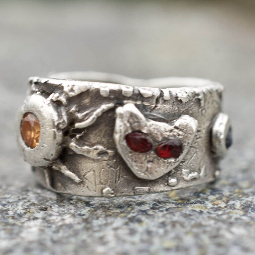 Detail prednej strany strieborného prsteňa JOYride so symbolmi slnka, mačky a nápisom JOY