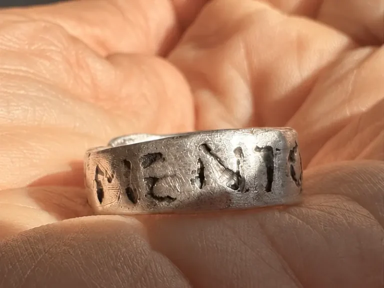 Detail autorského strieborného prsteňa na dlani s časťou nápisu Memento.